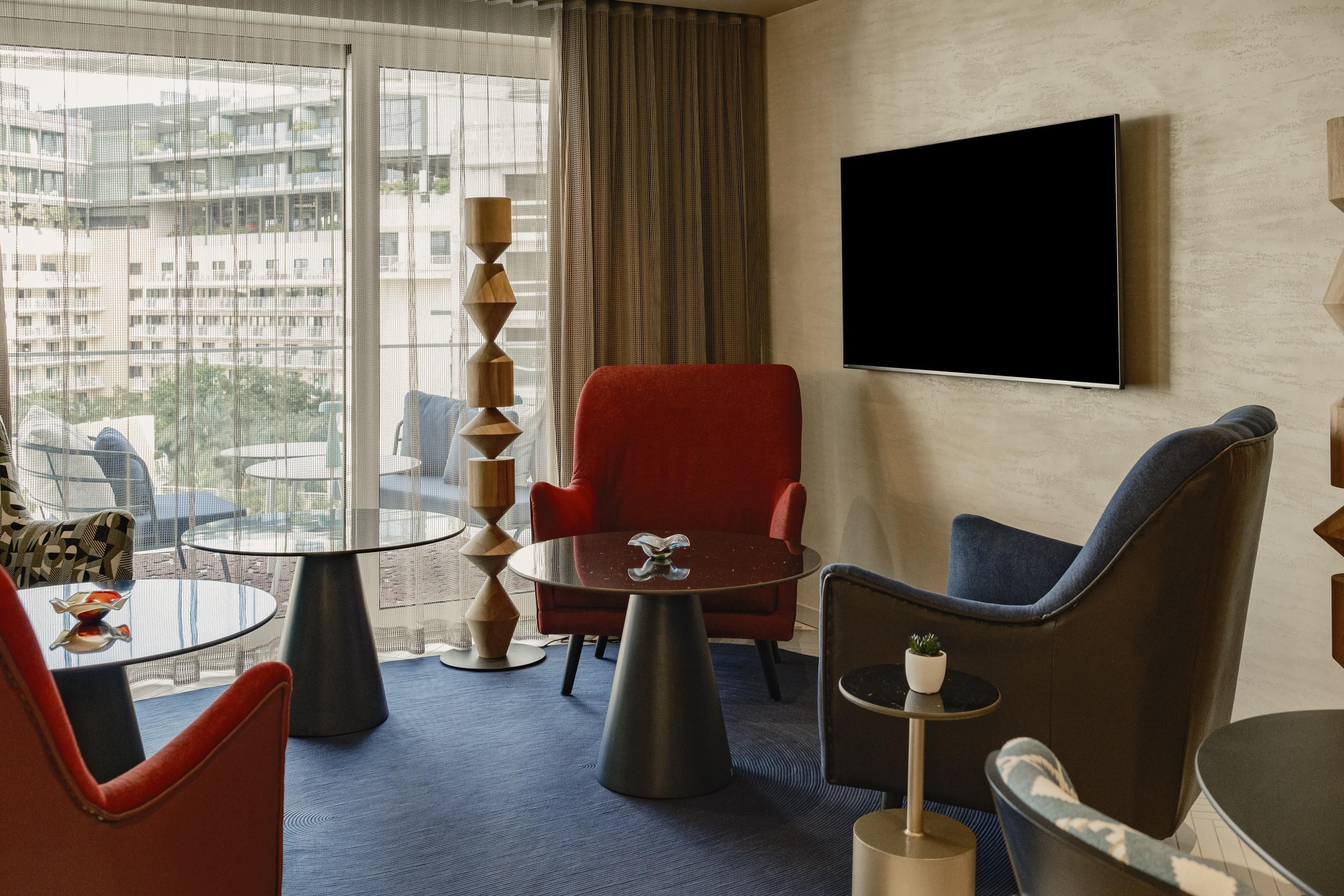 Une chambre d’hôtel moderne dotée d’une grande fenêtre, d’un téléviseur à écran plat, d’une table ronde et de deux chaises.