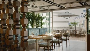 A modern indoor seating area with round tables, cushioned chairs, and a decorative wooden structure. - Hyatt Centric Malta (St. Julian's)