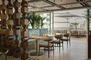 Un espace de détente intérieur moderne, avec des tables rondes, des chaises rembourrées et une structure décorative en bois.