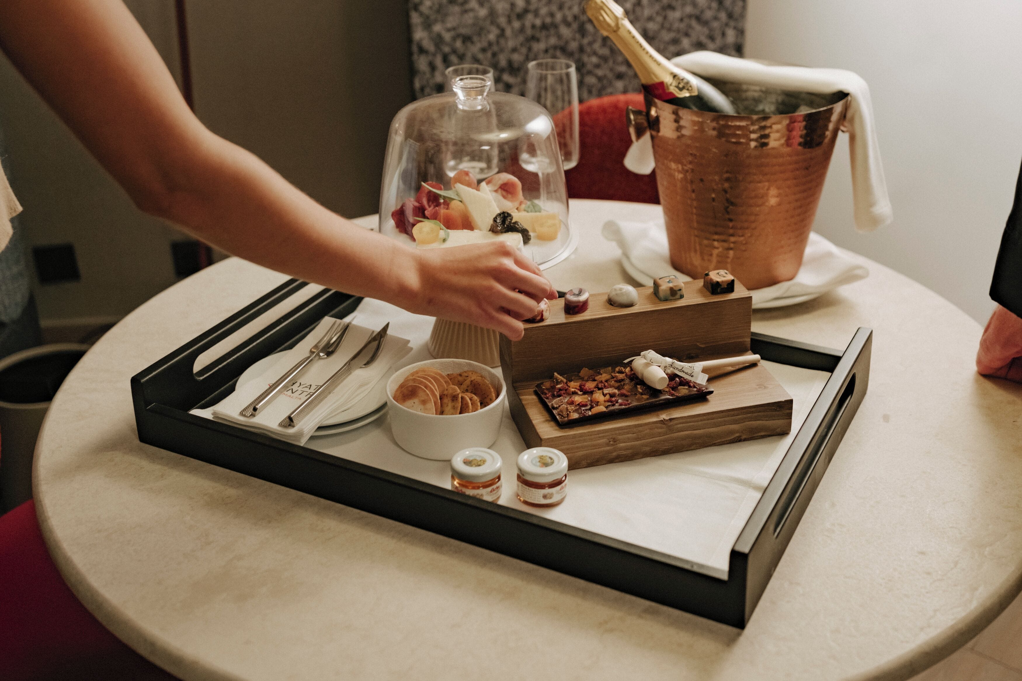 A table set with a bottle of champagne, a glass, a wooden tray with food, and a bowl of crackers.