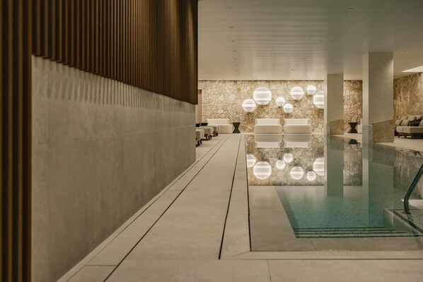 A modern indoor swimming pool with a stone wall and circular light fixtures.