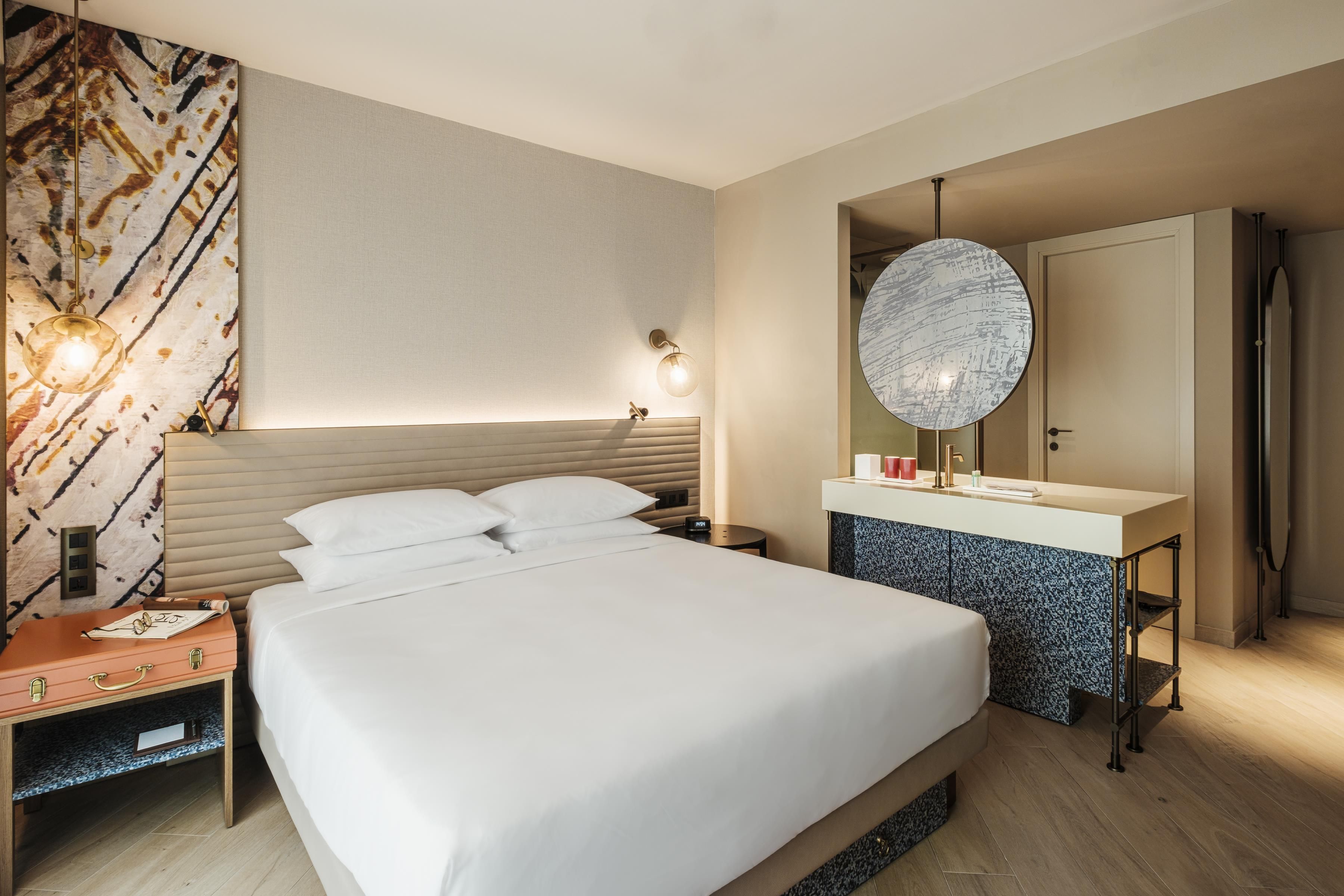 Una habitación de hotel con cama, mesita de noche y baño con espejo y lavamanos.