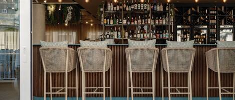 Una zona de bar con sillas de mimbre, una barra de madera y una variedad de botellas.