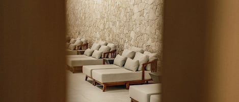 Un cuarto de spa con varias zonas de estar acolchadas frente a una pared de piedra con textura.