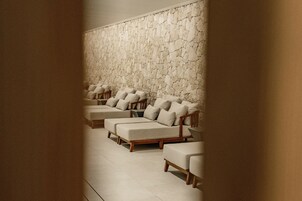 Un cuarto de spa con varias zonas de estar acolchadas frente a una pared de piedra con textura.