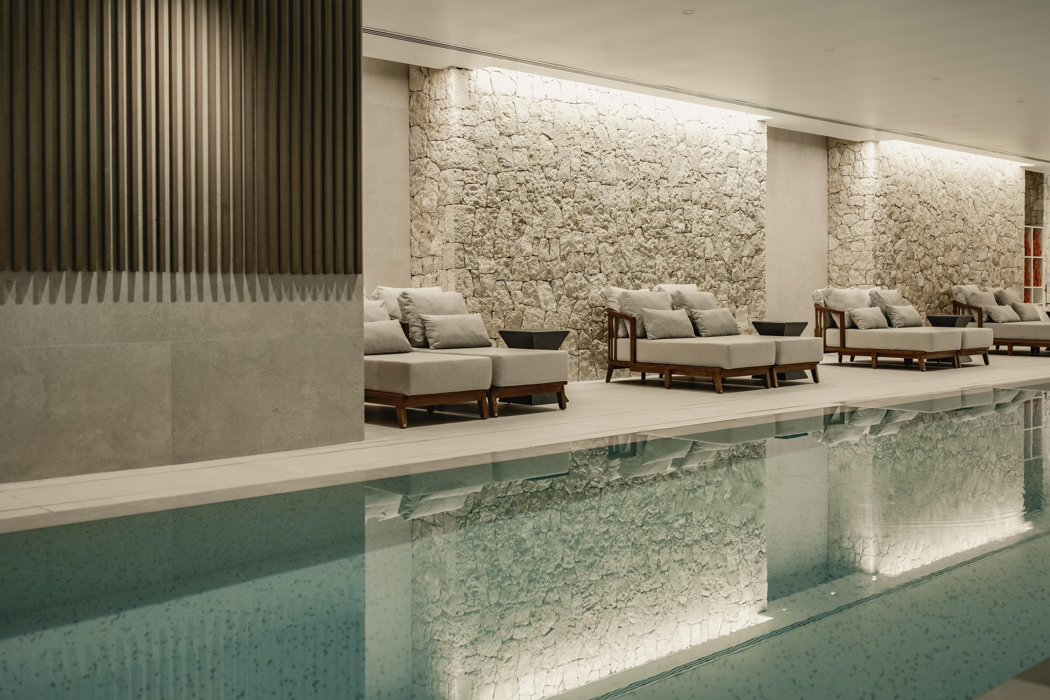 Un área junto a la piscina con sillones de descanso y un muro de piedra.