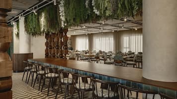 A bar area with a long counter, multiple chairs, and hanging greenery.