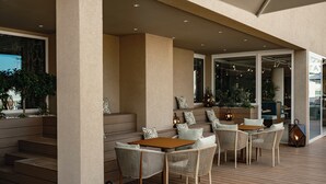 A covered outdoor seating area with wicker furniture and a wooden table, surrounded by steps and potted plants. - Hyatt Centric Malta (St. Julian's)