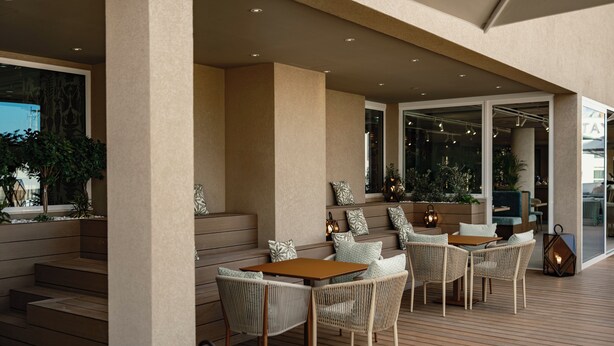 A covered outdoor seating area with wicker furniture and a wooden table, surrounded by steps and potted plants. - Hyatt Centric Malta (St. Julian's)