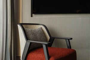 Una silla con respaldo tejido y asiento rojo, ubicada frente a una pared con paneles verticales y un televisor montado encima.