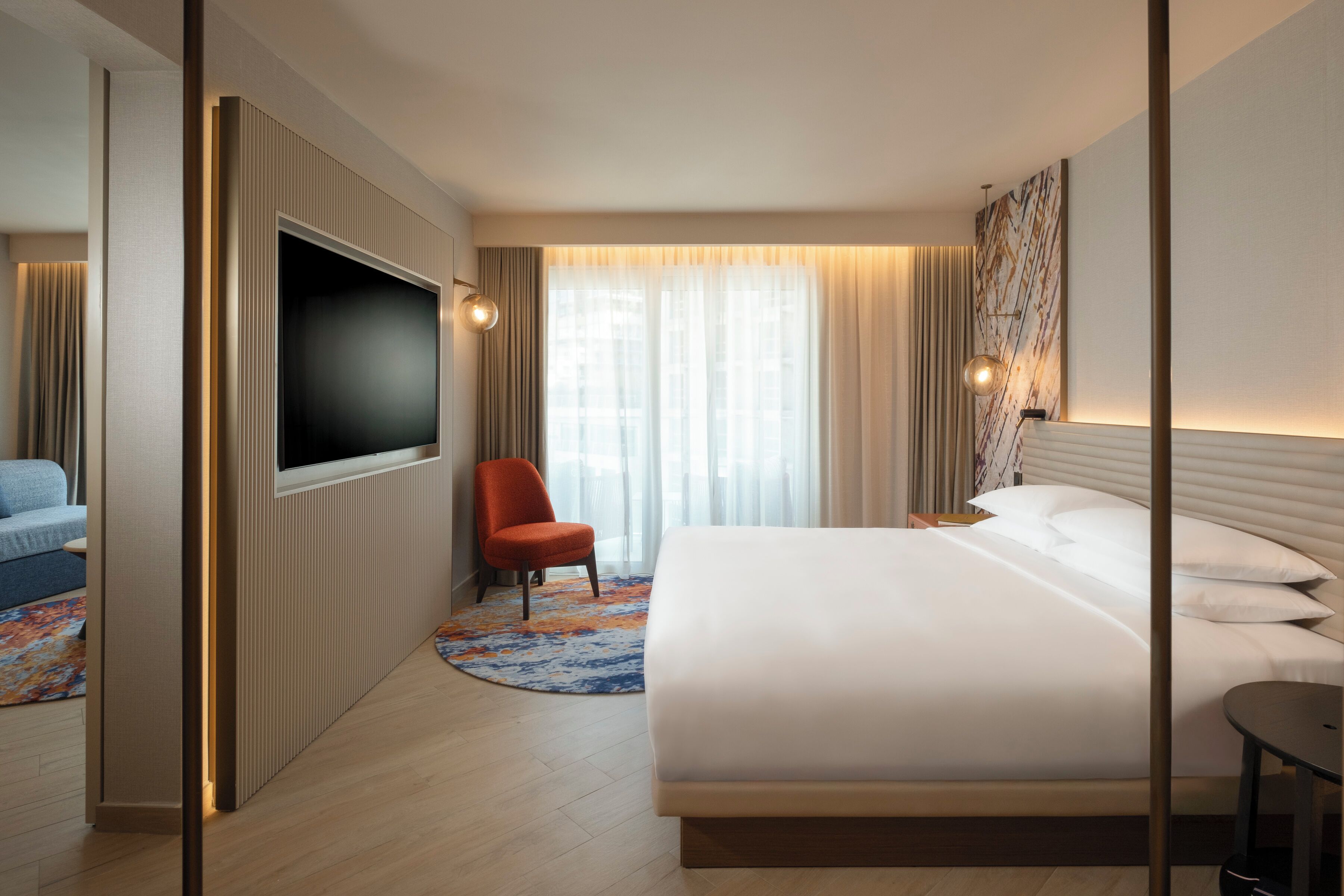 Une chambre d’hôtel avec un grand lit, un téléviseur à écran plat, un fauteuil rouge et un tapis à motifs.