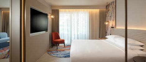 A hotel room with a large bed, a flat-screen TV, a red chair, and a patterned rug.