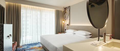 A hotel room with a bed, a bedside table, a mirror, a bathroom with a sink, and a window with curtains.