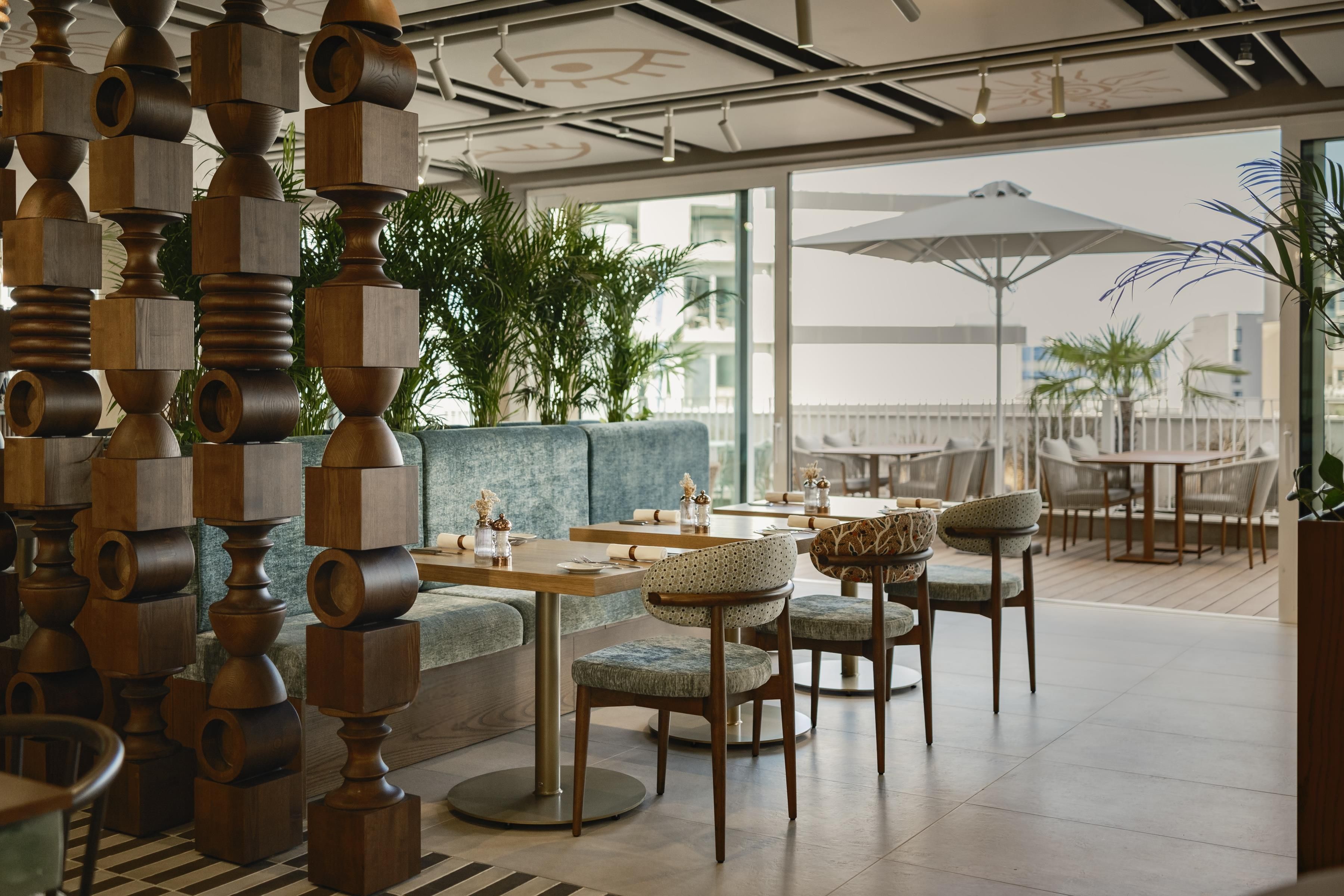 Un área de estar moderna en el interior, con mesas redondas, sillas acolchadas y una estructura decorativa de madera.