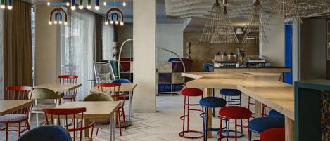 A modern restaurant interior with wooden tables, red and blue bar stools, and unique hanging light fixtures.