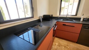 Une cuisine moderne avec des plans de travail noirs, des armoires orange, une cuisinière intégrée et une fenêtre donnant sur l’extérieur.
