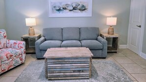 Una sala de estar con un sofá gris, un sillón estampado, una mesa de centro y dos lámparas sobre mesitas de noche.