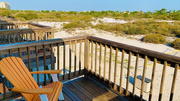 Terraza de madera con vista a una playa y edificios a lo lejos.