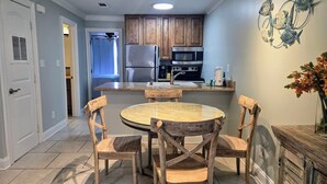 Una cocina con armarios de madera, un refrigerador de acero inoxidable, un microondas y un lavamanos. Hay una mesa de comedor con cuatro sillas.