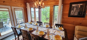A dining area with a table set for six, wooden walls, large windows, and a chandelier. - Lake Superior waterfront Cottage • Hot tub (Batchawana Bay)