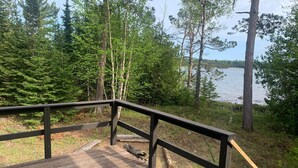 Eine Holzterrasse mit Geländer, die auf einen See mit umliegenden Bäumen blickt.
