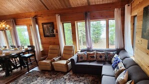Ein rustikales Holzhaus-Interieur mit einer Couch, Sesseln, einem Esstisch und großen Fenstern.