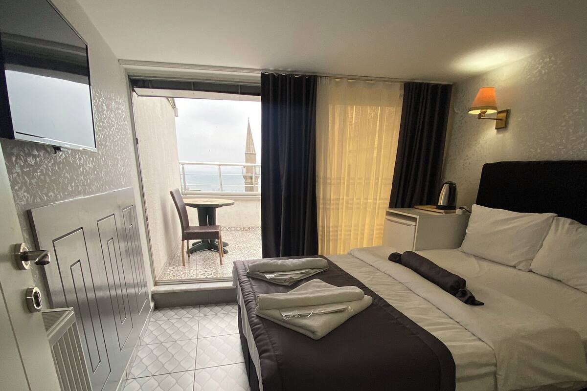 A hotel room with a bed, a small table, a chair, and a view of the outside.