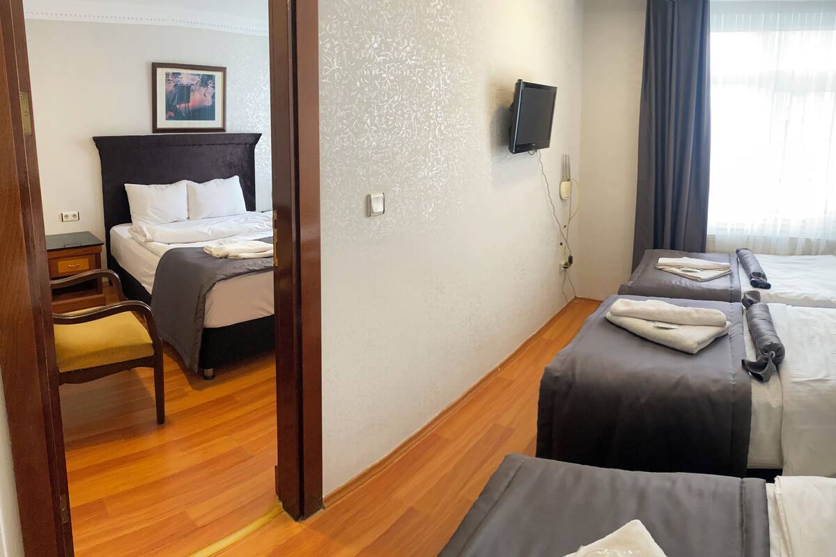 A hotel room with two beds, a wooden chair, a bedside table, a TV, and a window with curtains.