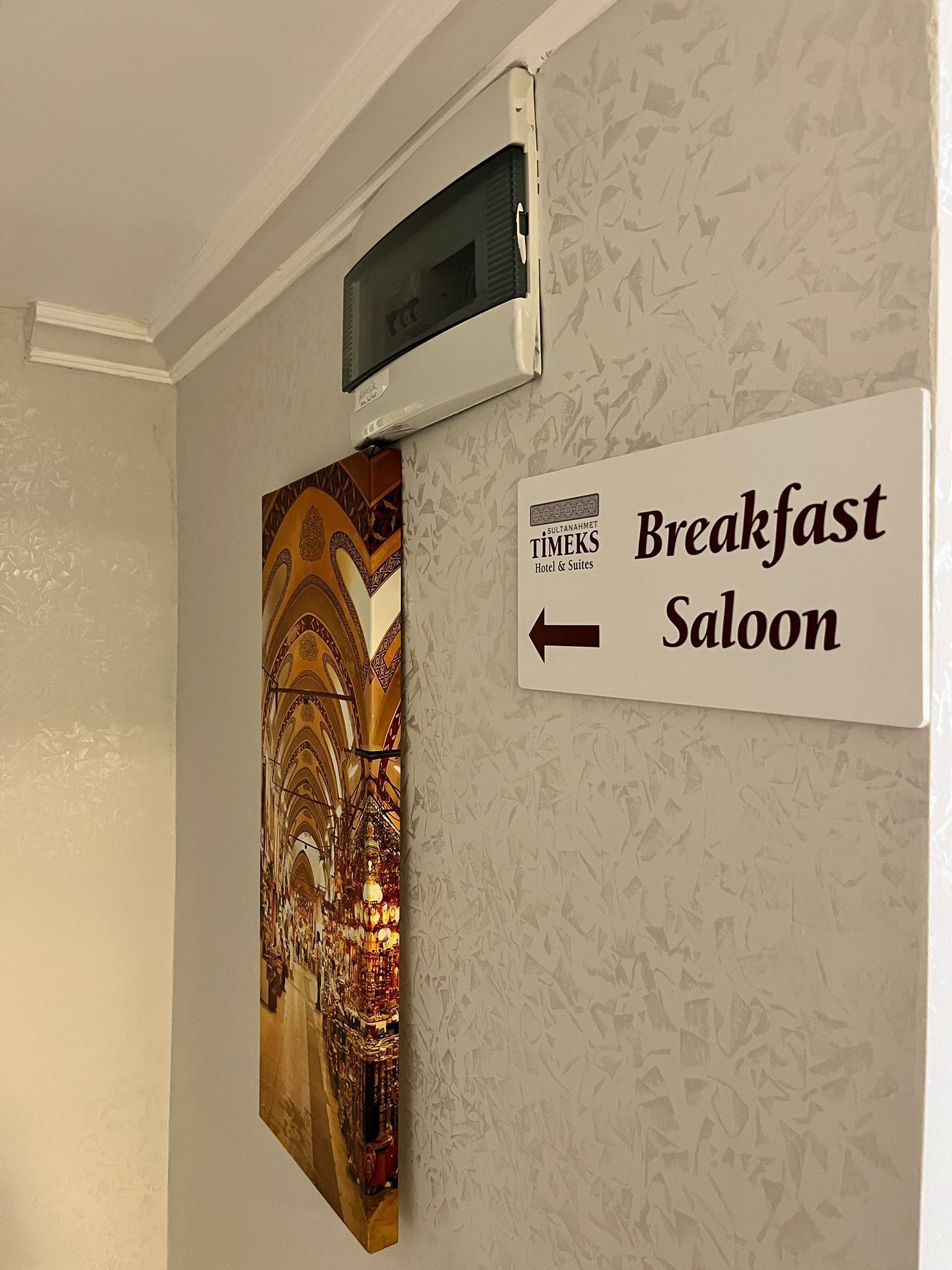 A wall with a sign indicating the direction to the breakfast saloon and a decorative painting.