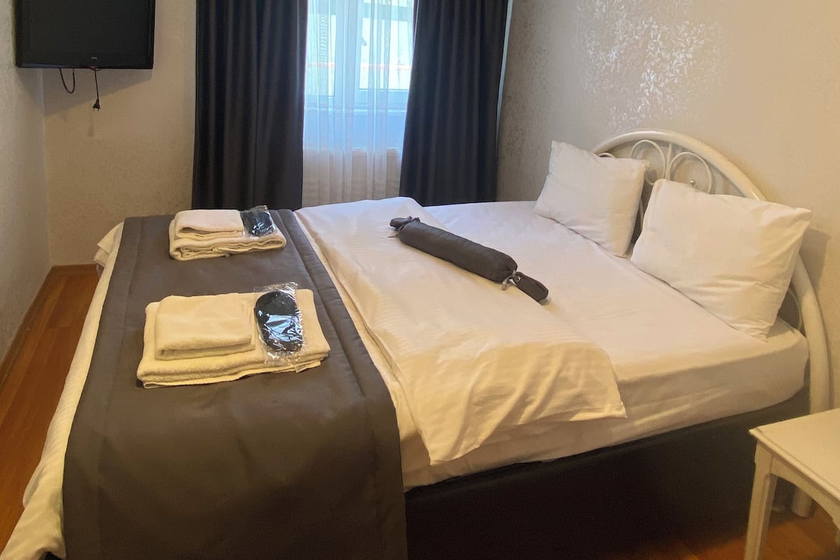 A hotel room with a bed, a TV mounted on the wall, and an air conditioning unit.