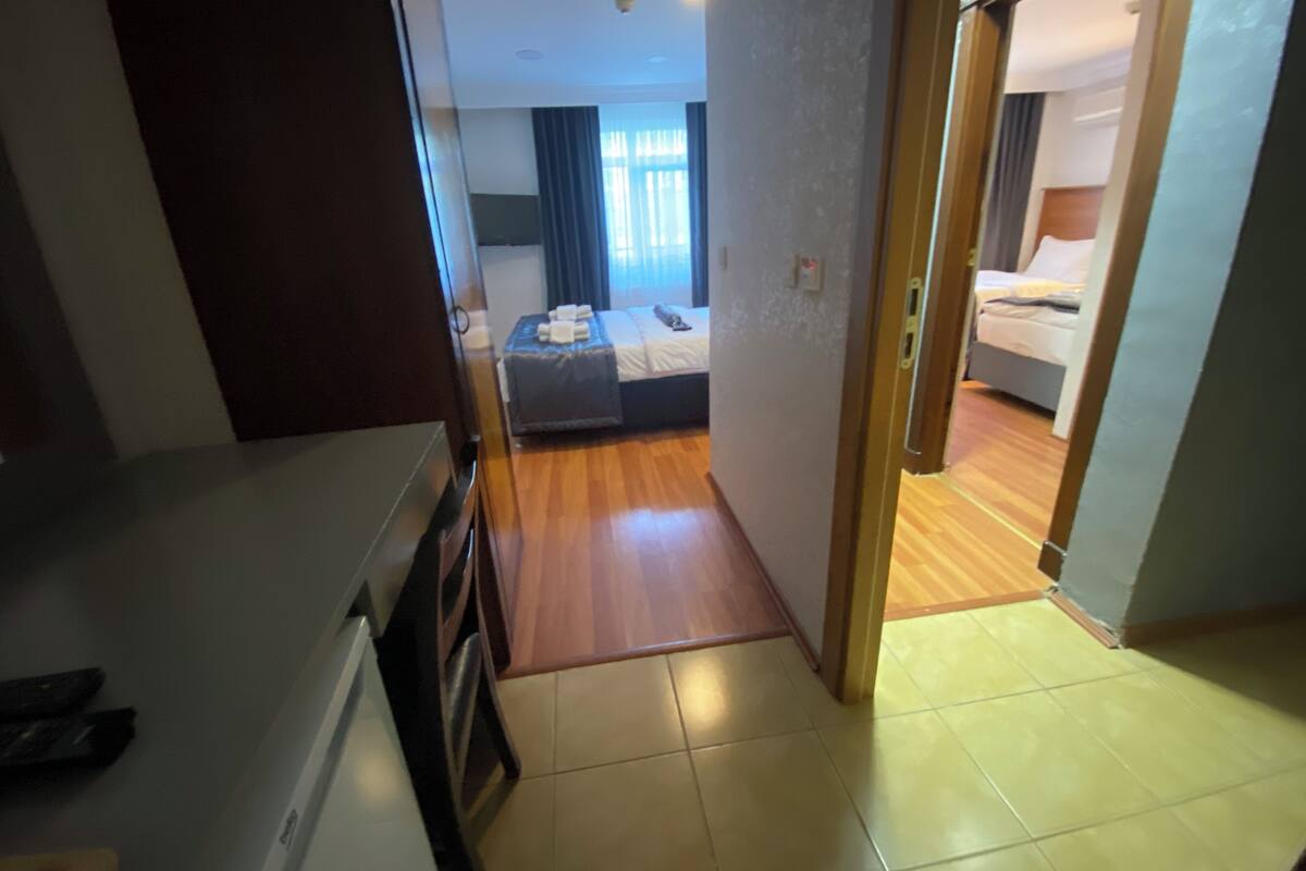 A hotel room with a bed, a desk, and a view of another room.