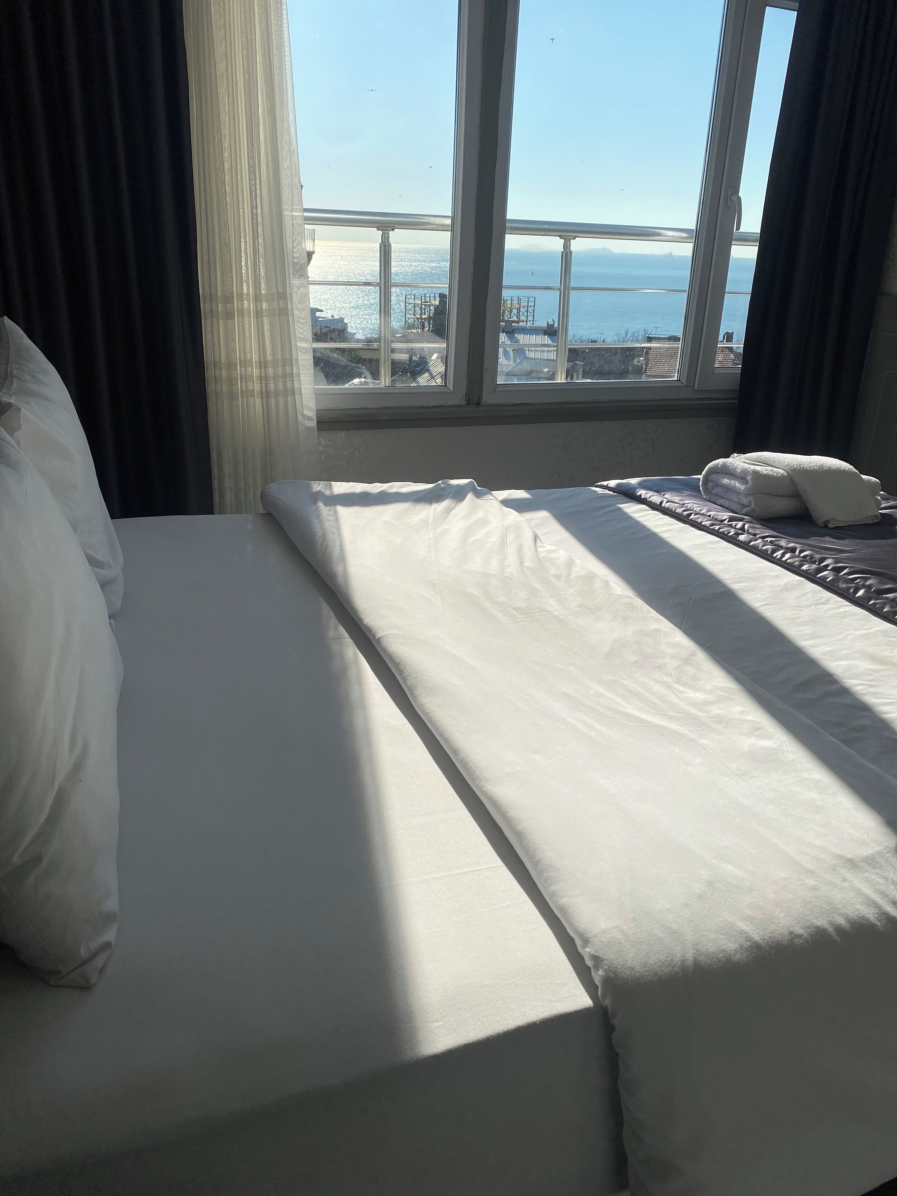 A hotel room with a bed, a view of the sea, and a window with curtains.