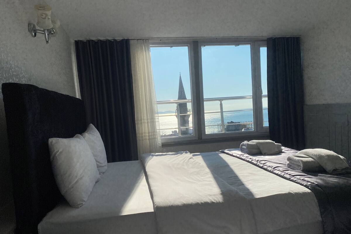 A hotel room with a bed, a view of a cityscape, and a window with curtains.