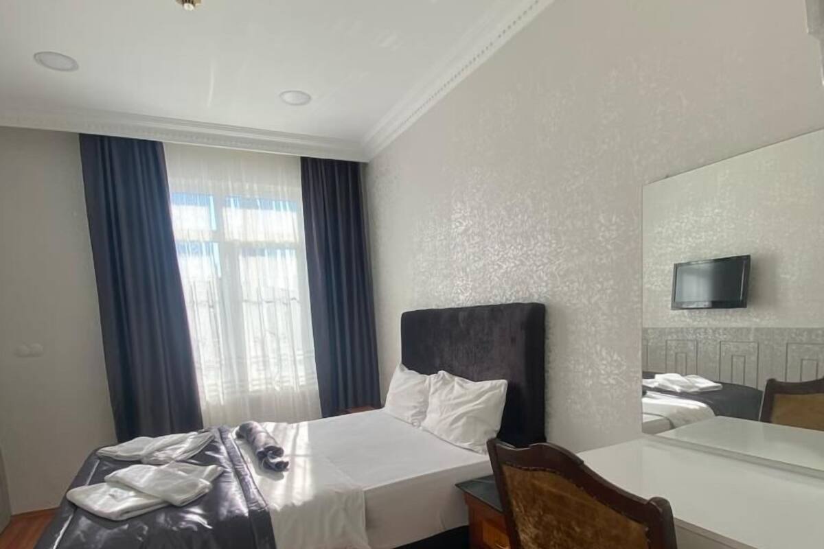 A hotel room with a bed, a desk, a chair, a TV, and a window with curtains.