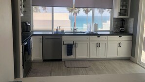 Cozinha com vista para o oceano, armários brancos, fogão preto e uma janela grande com vista.