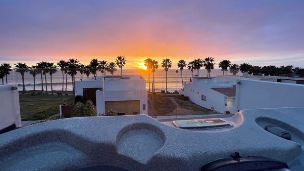 Um edifício moderno com piscina no terraço e vista para o pôr do sol sobre o oceano.