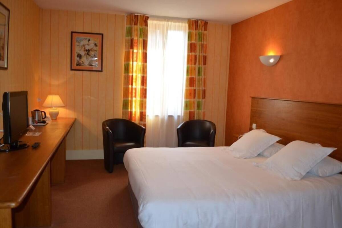 Een hotelkamer met een bed, twee stoelen, een bureau met een lamp, een televisie en een schilderij aan de muur.