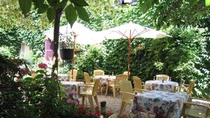 Un espace extérieur aménagé en terrasse, avec des tables et des chaises rondes, entouré d’une végétation luxuriante et de fleurs.
