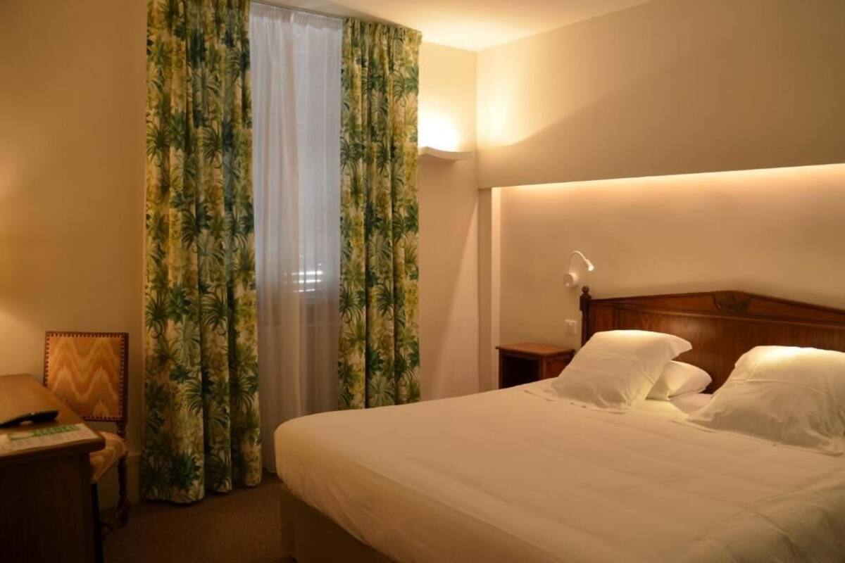 Een hotelkamer met een bed, nachtkastje, bureau en gordijnen.