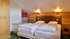 Ein Schlafzimmer mit hölzernem Kopfteil, zwei Betten mit weißer Bettwäsche, einem Nachttisch und einem Kleiderschrank.