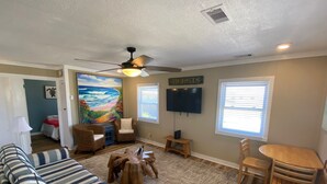 A living room with a striped sofa, a wooden coffee table, a ceiling fan, a TV, and a painting of a beach scene. - Cottage Close To Beach and abuts the Wright Brother Memorial (Kill Devil Hills)