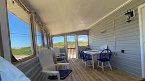 A covered outdoor deck with white chairs and a table, overlooking a scenic landscape. - Cottage Close To Beach and abuts the Wright Brother Memorial (Kill Devil Hills)