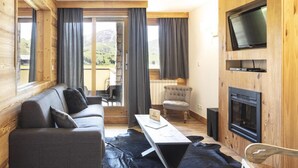 Una habitación acogedora con sofá, mesa, silla, chimenea y televisión montada en la pared.