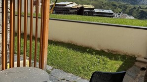 Un patio con una mesa y una silla, una cerca de madera y vistas a edificios y montañas al fondo.