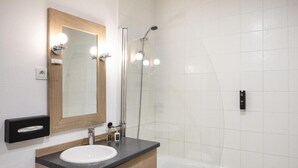 Un baño moderno con lavamanos blanco, tocador de madera, un espejo grande y ducha con cerramiento de vidrio.