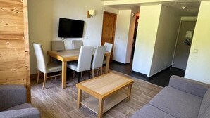 A modern living room with a wooden coffee table, grey sofas, and a dining area with a TV and chairs. - Ski-in/ski-out & foot of the slopes, 3rd floor, view ski slopes, swimming pool, balcony, tv (La Plagne)