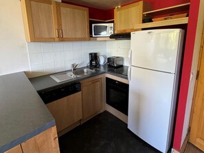 Una cocina compacta con armarios de madera, microondas, tostadora, cafetera, lavamanos y refrigerador.