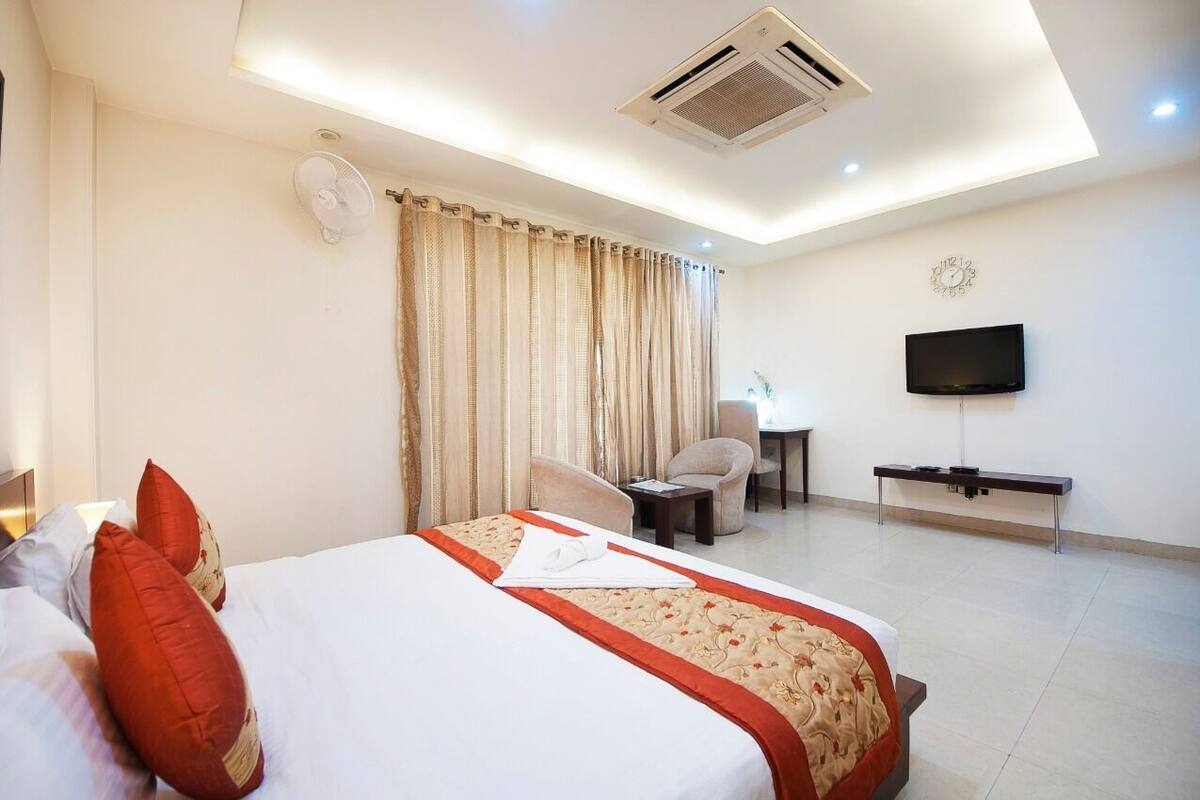 A hotel room with a bed, a desk, a chair, a TV, and a clock on the wall.