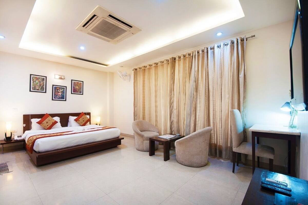 A modern hotel room with a large bed, two armchairs, a small table, and a desk with a lamp.