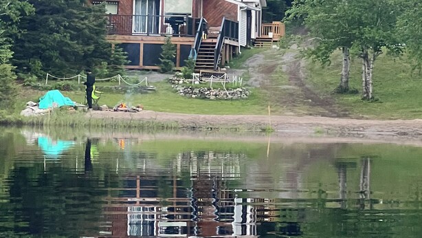Een chalet met terras, uitkijkend over een meer, omringd door bomen.